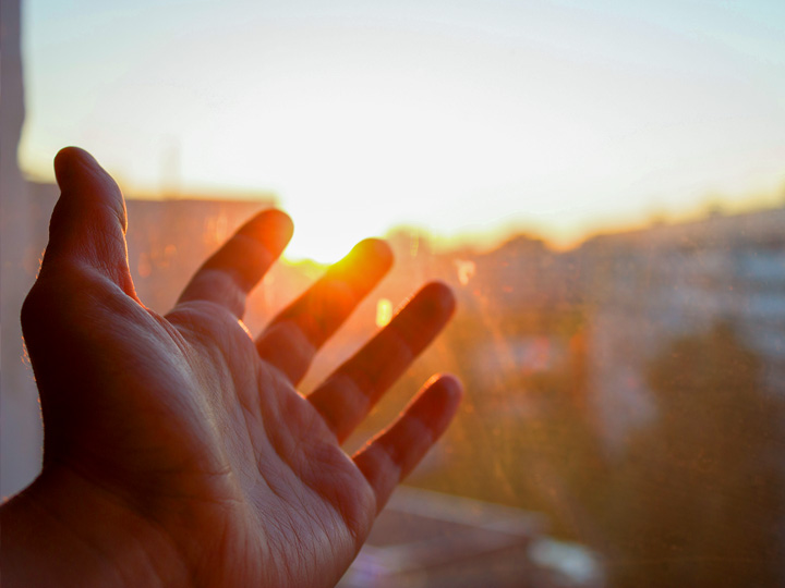 Hand reaching toward sun symbolizing hope of reaching goals